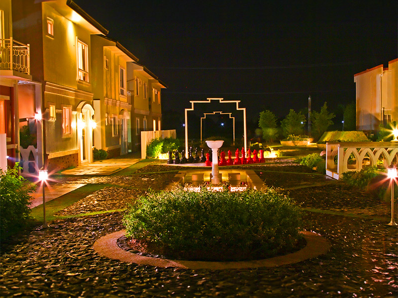 Lancaster New City Cavite illuminated courtyard at night, with landscaped gardens, elegant walkways, decorative fountains, and English Countryside inspired homes creating a peaceful community setting.